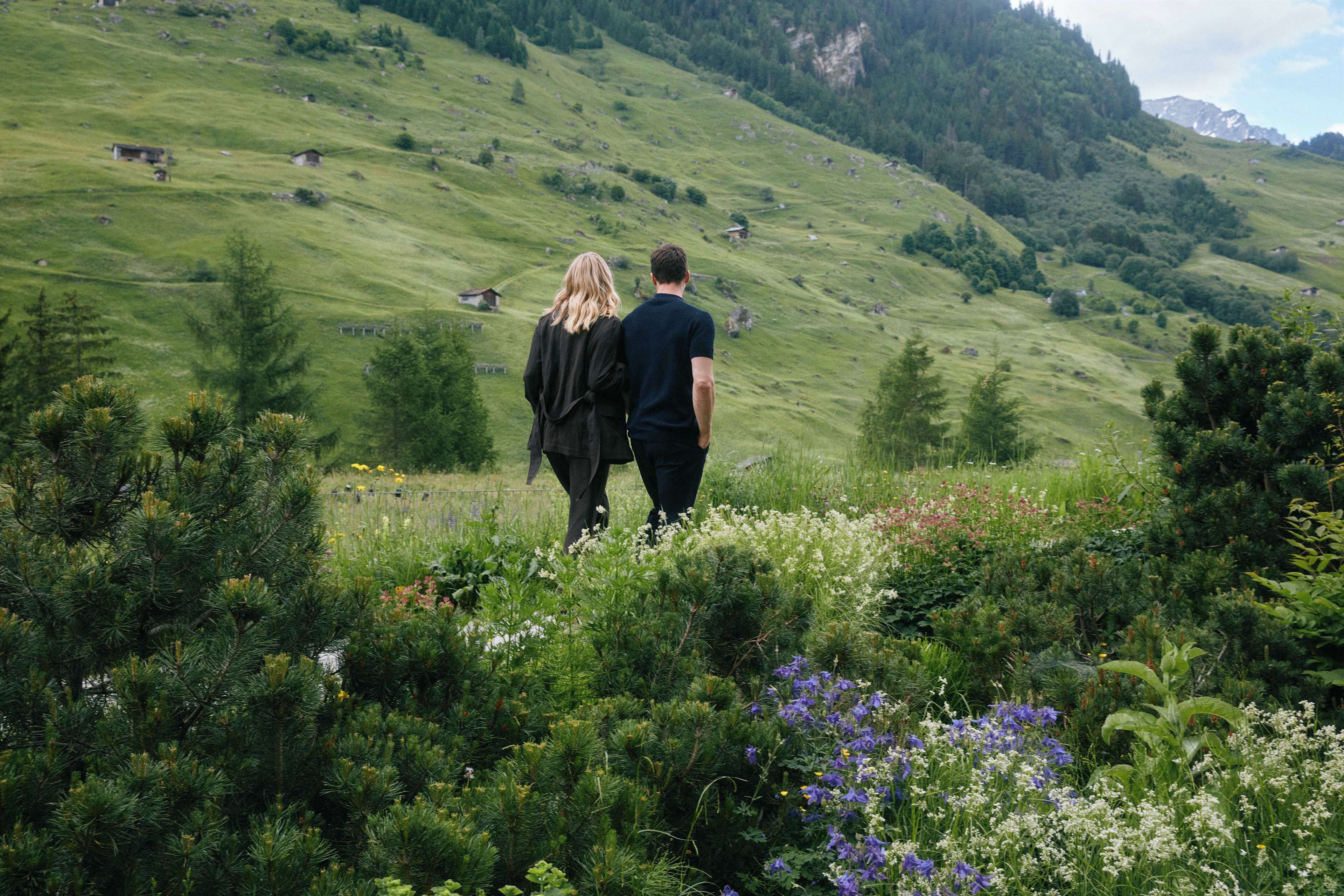 A couple walking on a grassy hillside with a view of a mountain in the background.