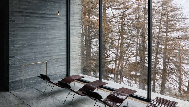 A modern interior with large windows, a minimalist design, and a view of a snowy forest. - 7132 Hotel (Vals)