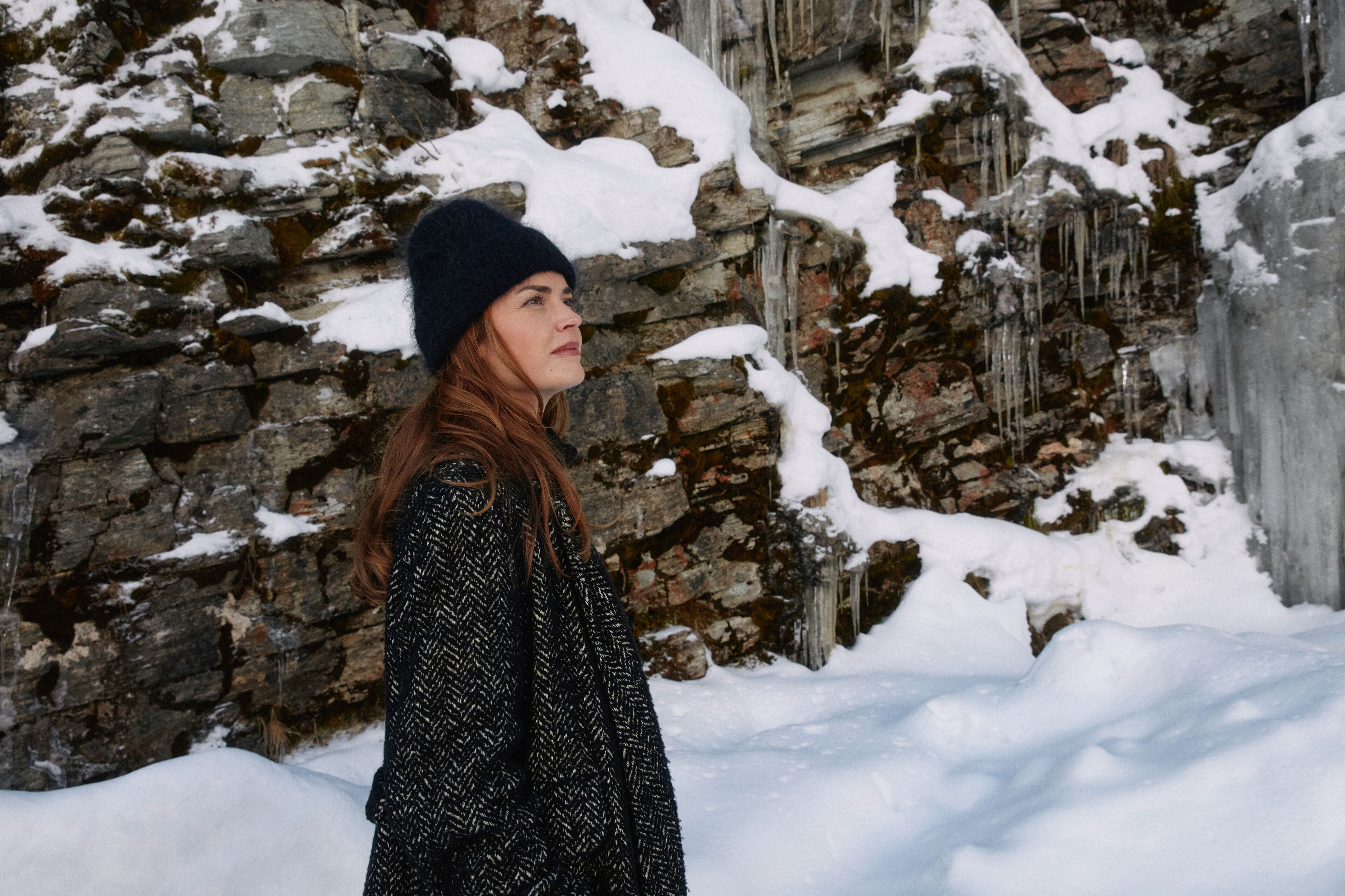 Una persona parada en un espacio exterior nevado con un muro de piedra y estalactitas.