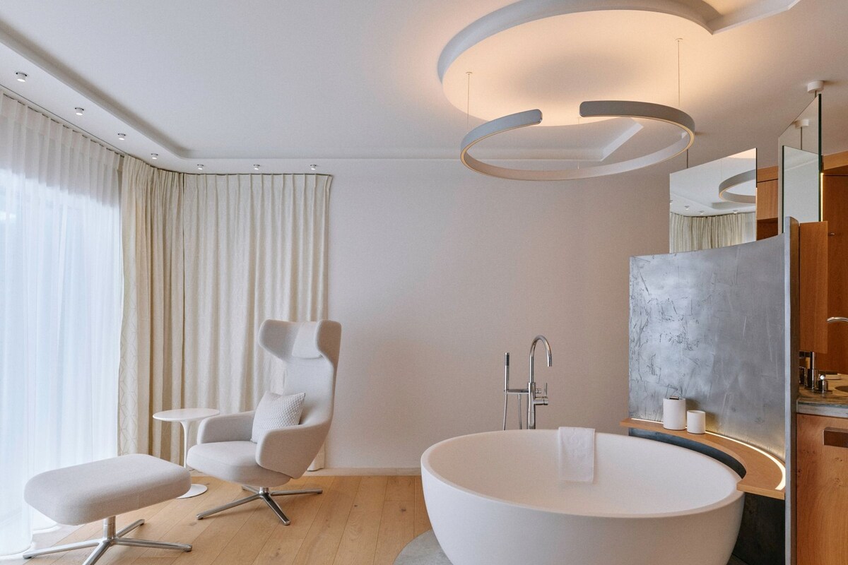 A modern bathroom with a freestanding bathtub, a chair, and a vanity with a mirror.