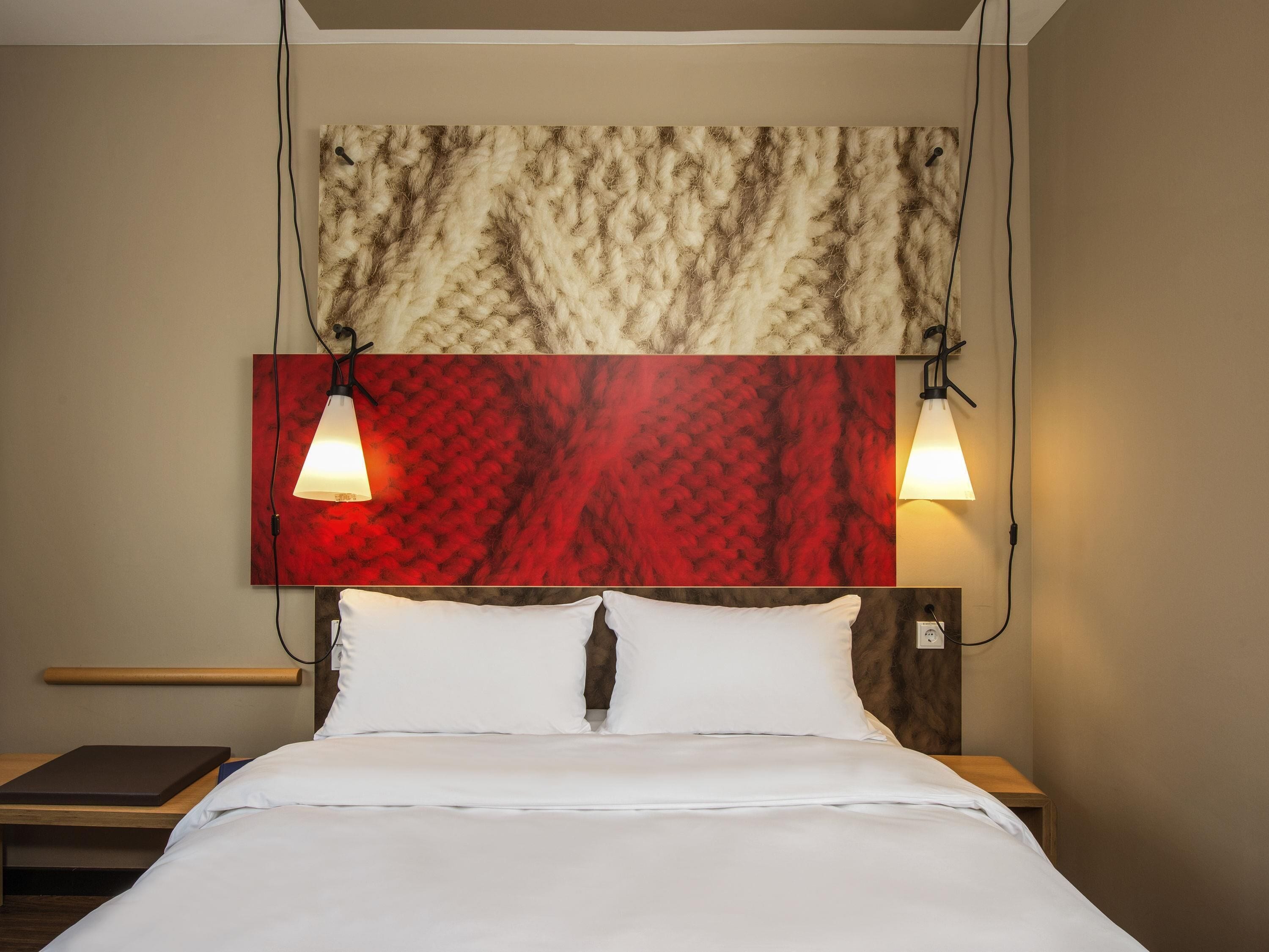 A hotel room with a bed, two bedside lamps, a wooden bedside table, and a headboard with a textured design.