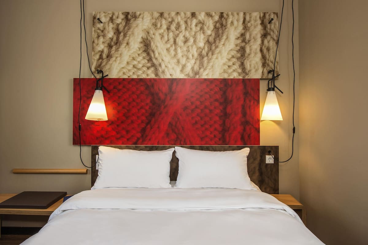 A hotel room with a bed, two bedside lamps, a wooden bedside table, and a headboard with a textured design.