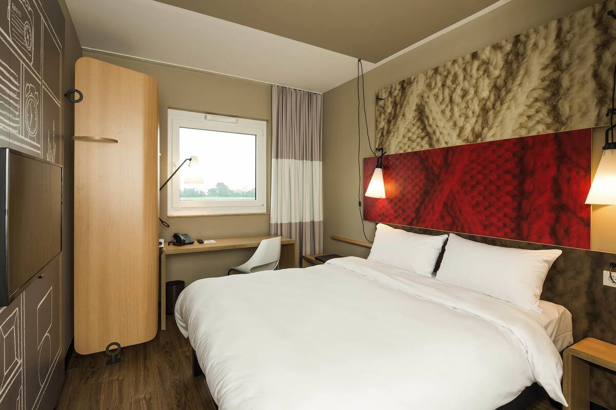 Hotellihuone, jossa on sänky, työpöytä, tuoli ja ikkuna, jossa on verhot.