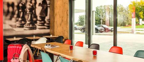 A conference room with a long table, colorful chairs, and a large window with a view of parked cars and trees.
