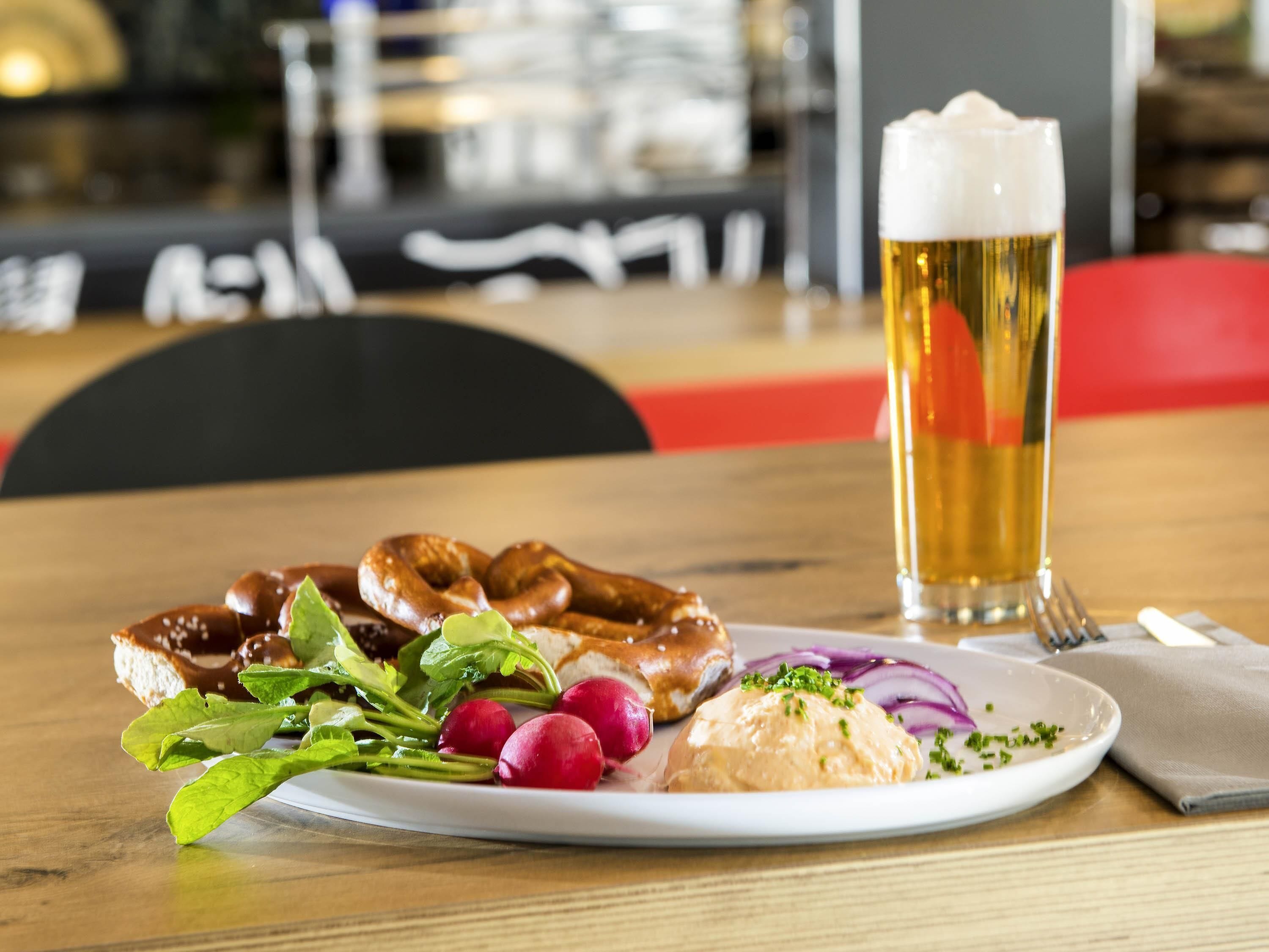 Un piatto con bretzel, ravanelli e verdure, e un bicchiere di birra su un tavolo di legno.
