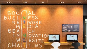 En reception med en opslagstavle dækket af forskellige ord relateret til erhvervslivet, to computorskærme og to stole.