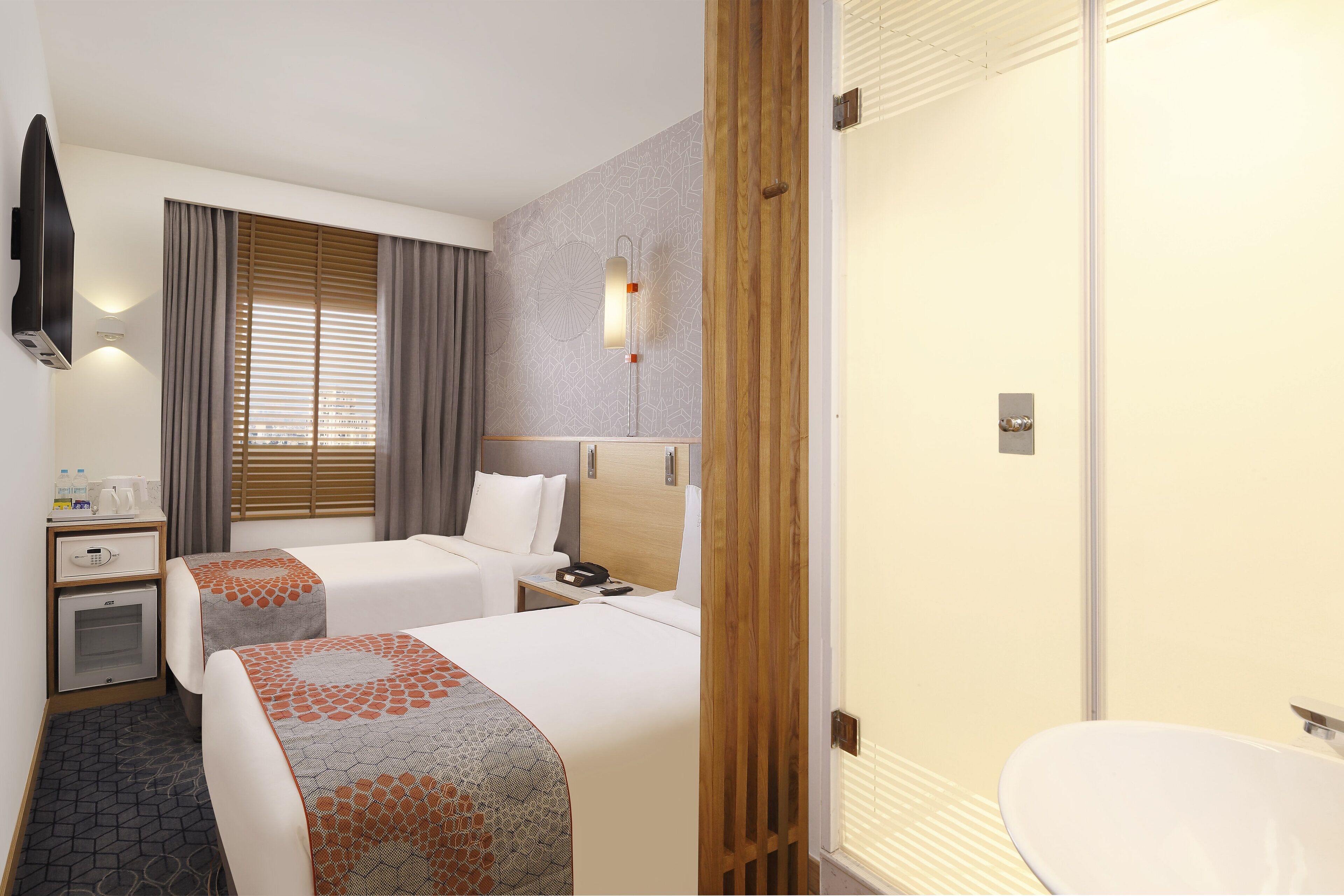 Habitación de hotel con dos camas, una mesita de noche con lámpara, un armario y un baño con lavamanos e inodoro.