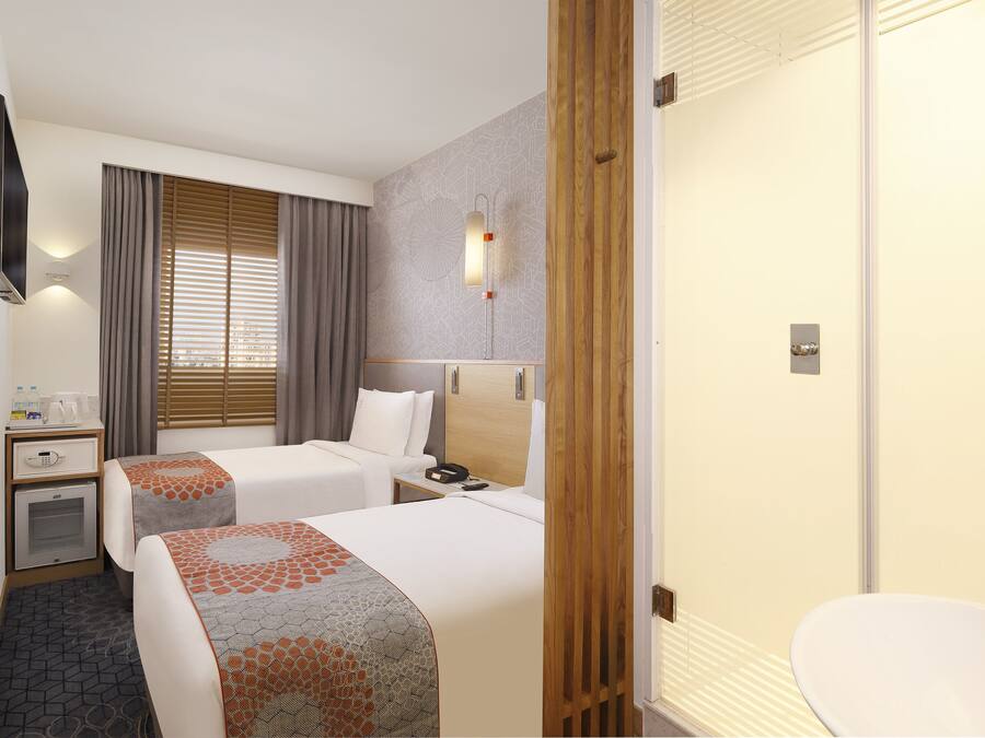 Habitación de hotel con dos camas, una mesita de noche con lámpara, un armario y un baño con lavamanos e inodoro.
