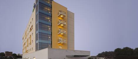 Un hotel moderno con fachada amarilla, varios balcones y entrada de vidrio.