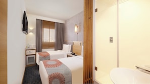 A hotel room with two beds, a desk, a minibar, a bathroom with a toilet and sink, and a window with blinds.