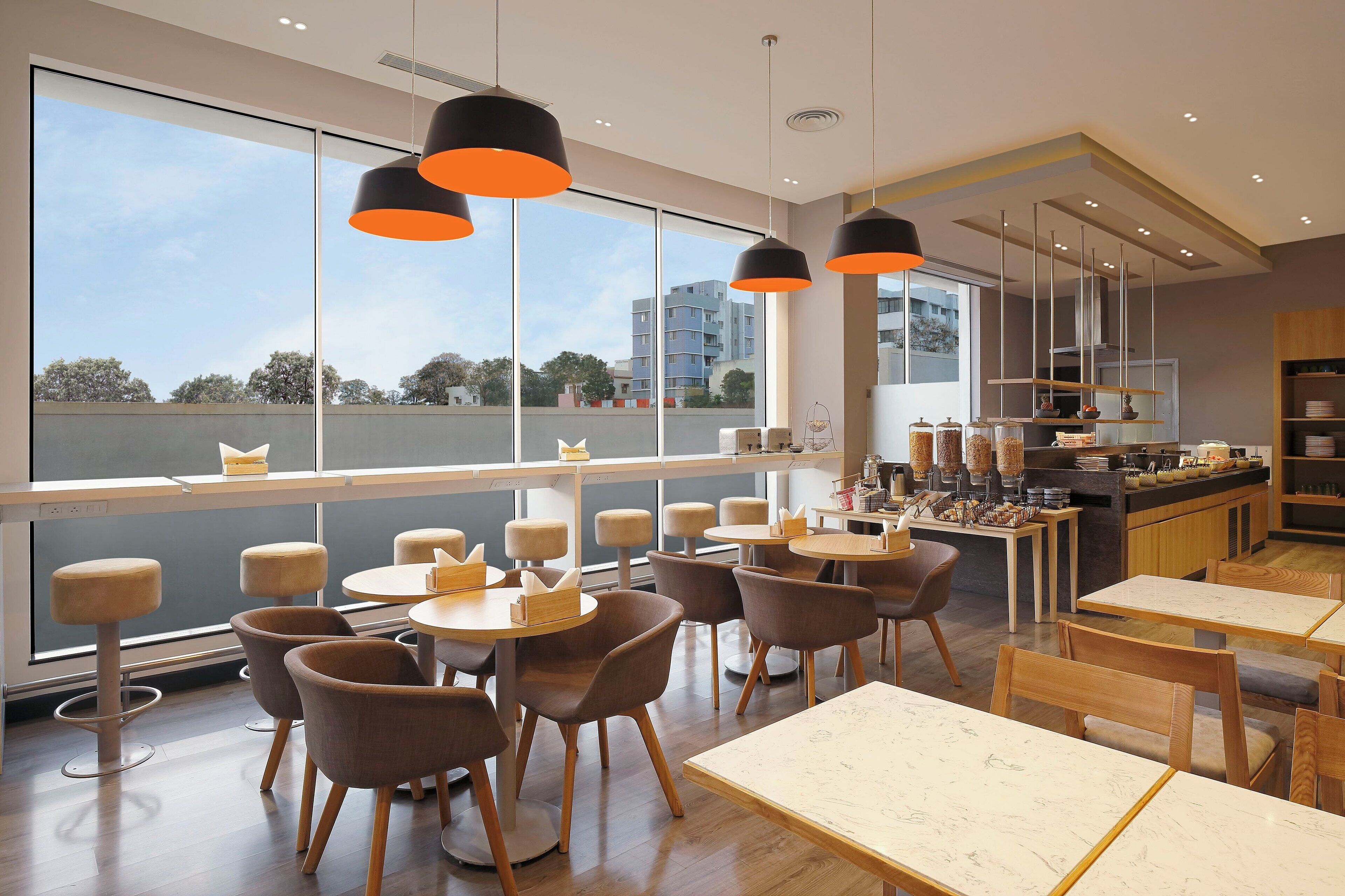 A modern dining area with tables and chairs, large windows, and a view of buildings outside.