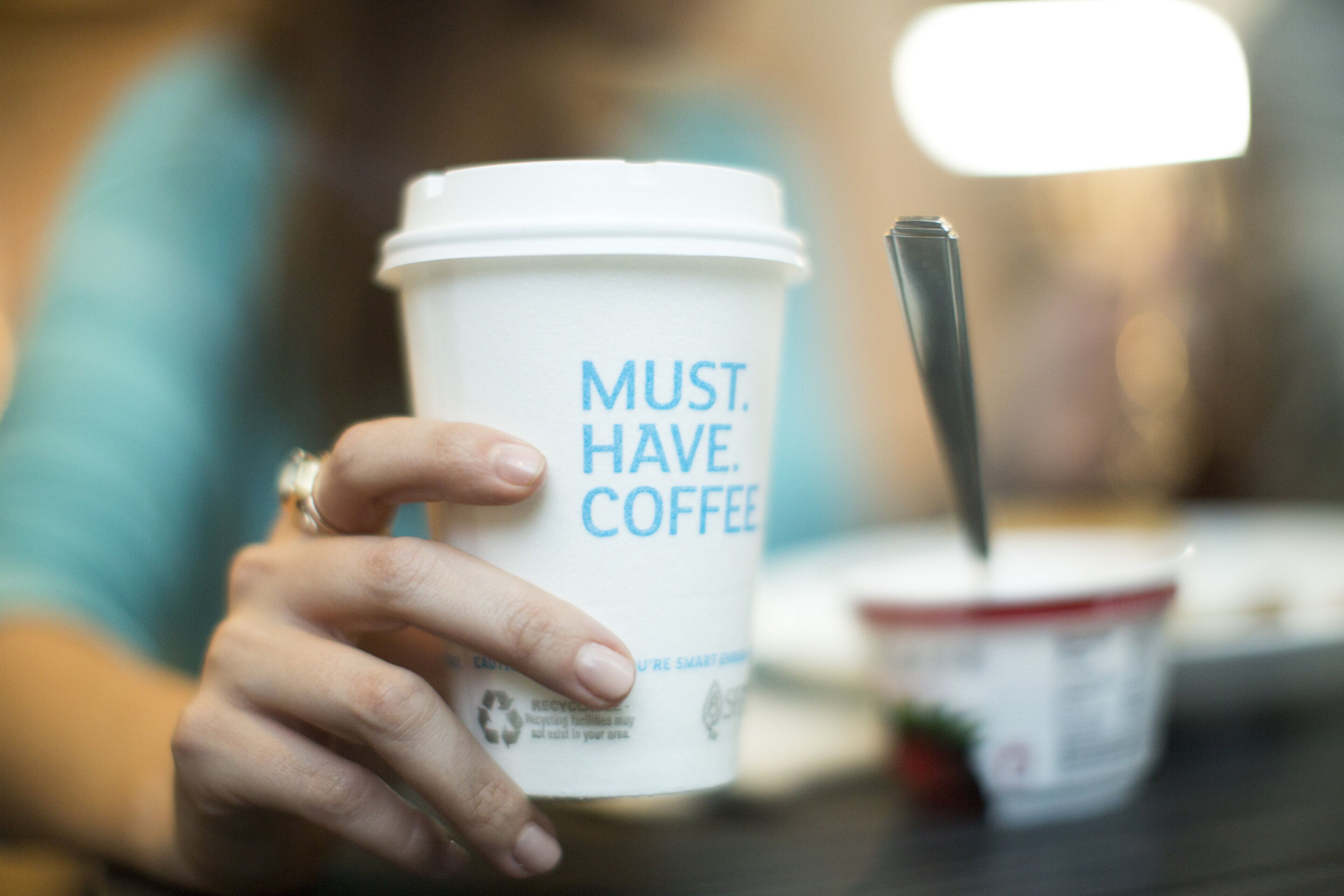 A hand holding a coffee cup with the text "MUST. HAVE. COFFEE."