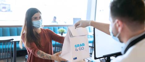 A person handing over a paper bag with 'GRAB & GO' text to another individual.