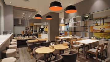 A modern cafe with multiple seating areas, including round tables and bar stools, and a counter with a variety of food items.