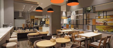A modern cafe with multiple seating areas, including round tables and bar stools, and a counter with a variety of food items.