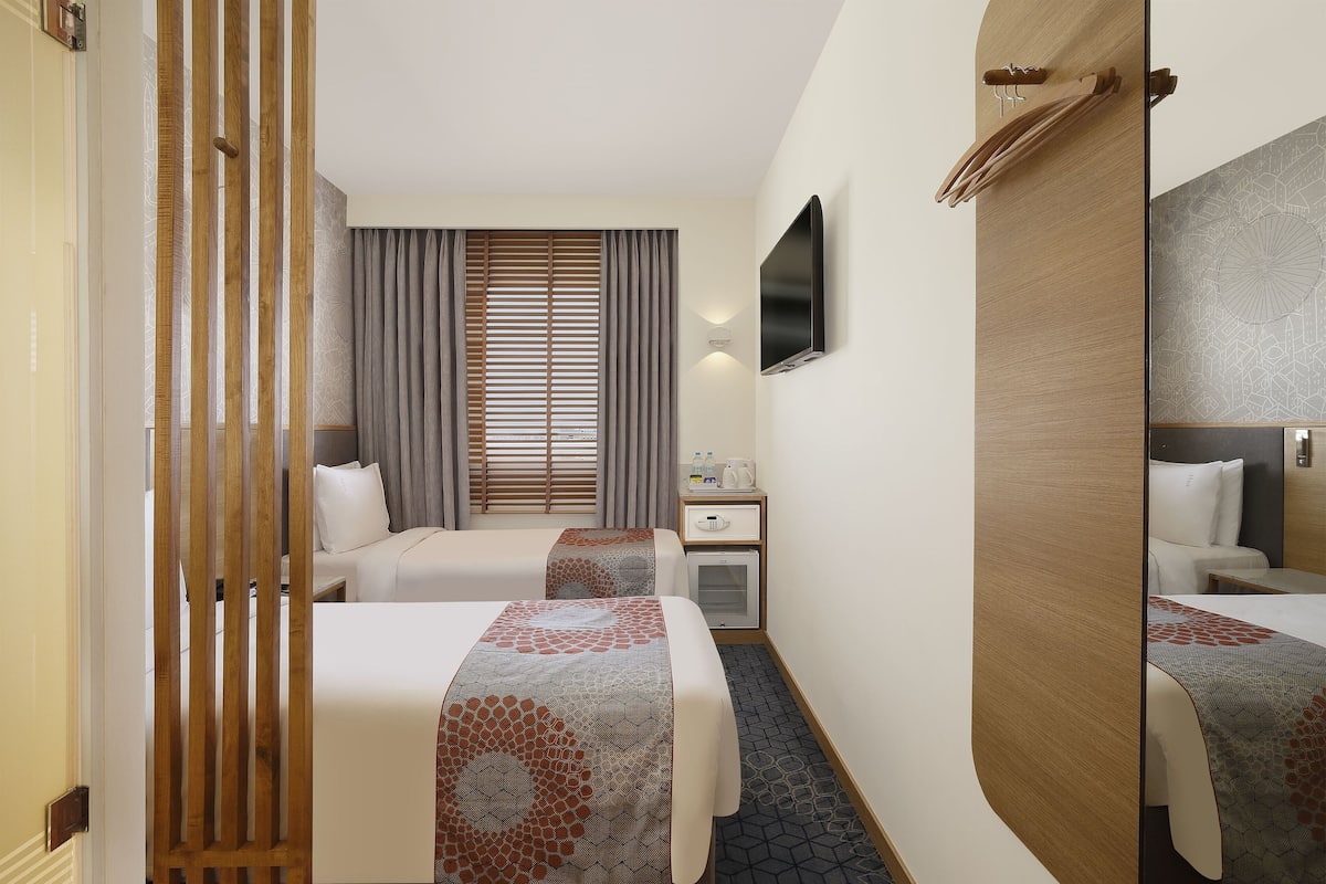 A hotel room with two beds, a desk, a TV, and a wardrobe.