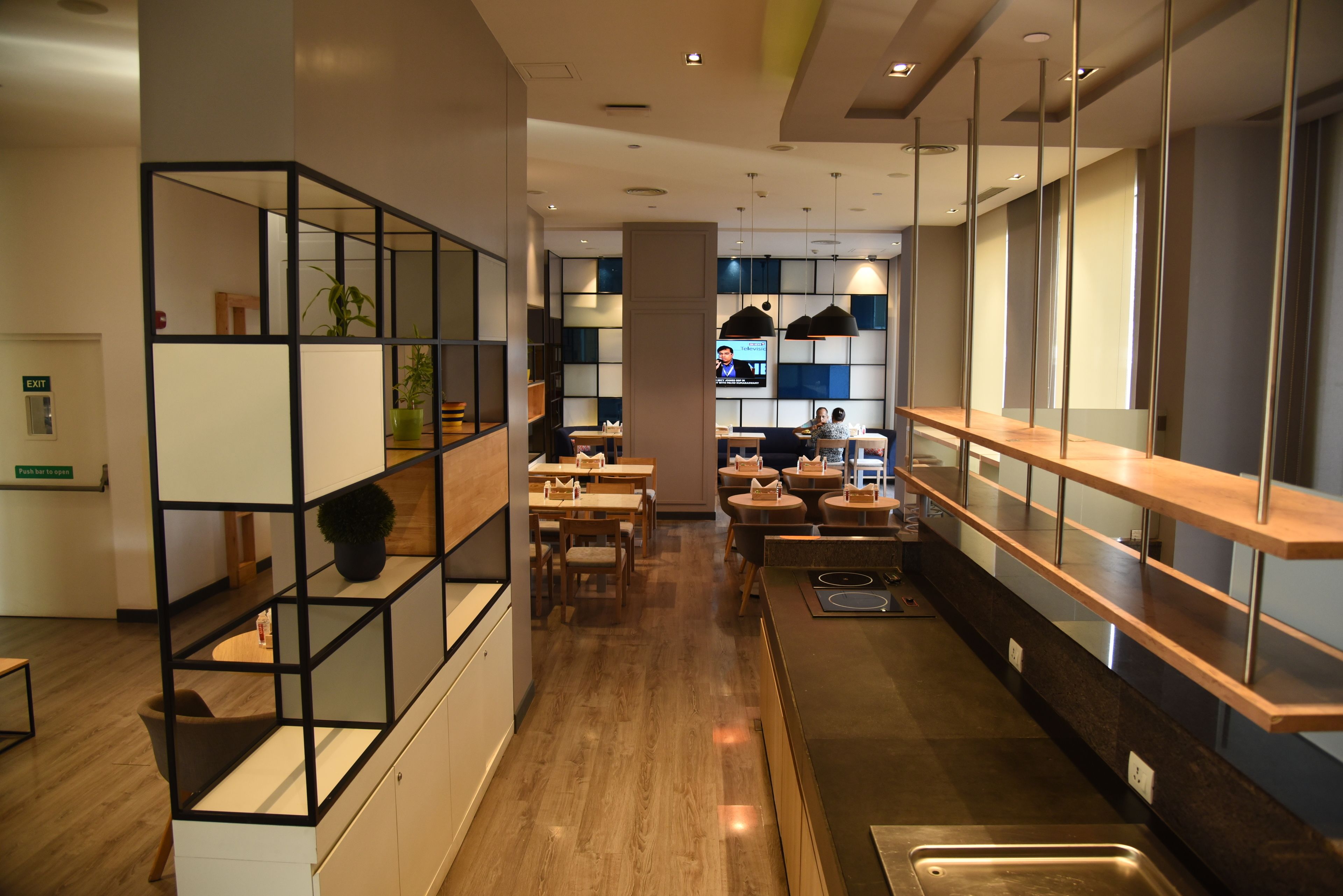 A modern hotel lobby with a central seating area, a reception desk, and a TV screen displaying a program.