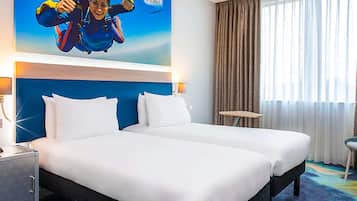A hotel room with a large bed, a headboard, a nightstand, a lamp, a small table, and a window with curtains.