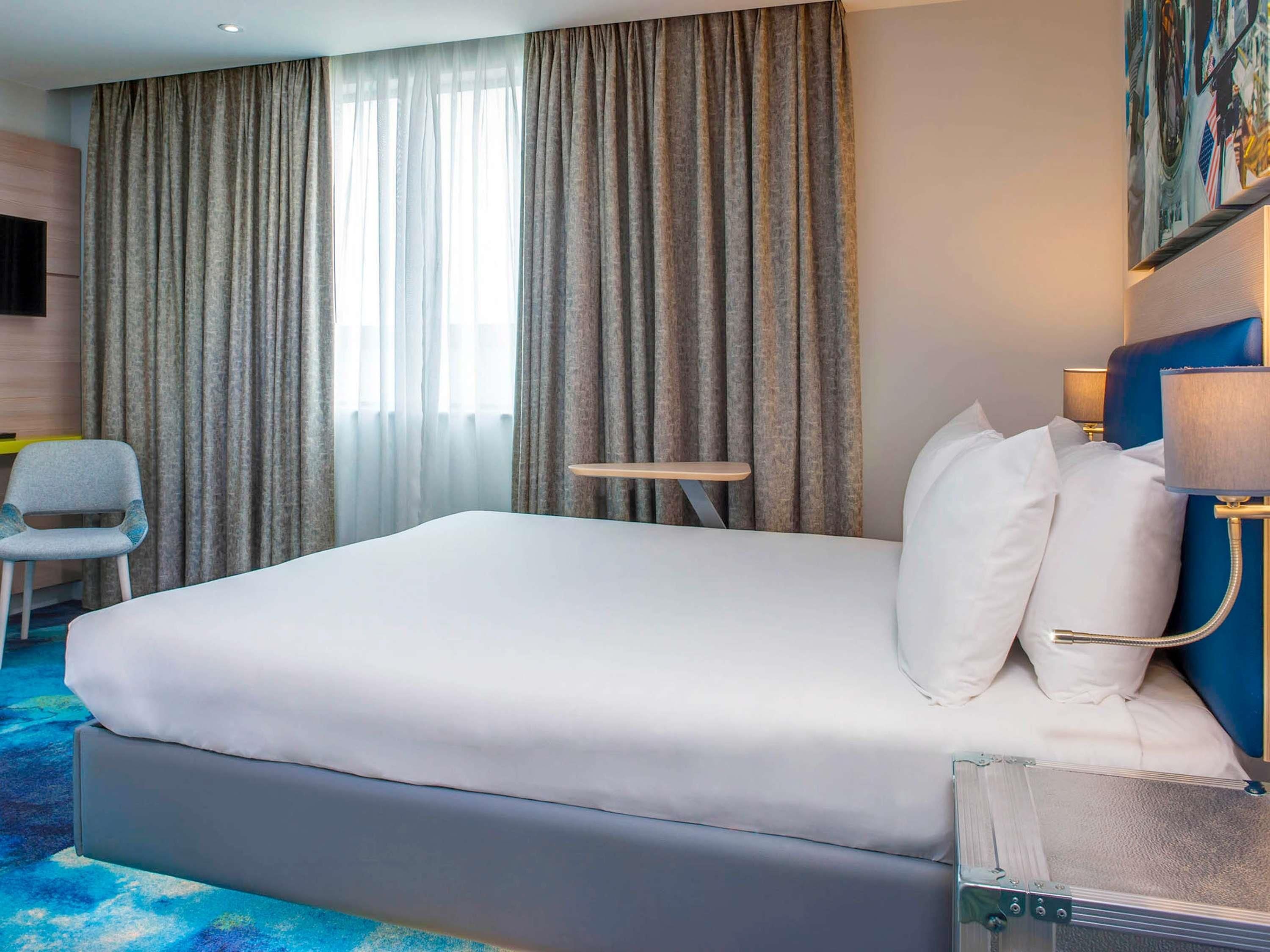 Une chambre d’hôtel avec un grand lit, une petite table, une chaise et un téléviseur fixé au mur.
