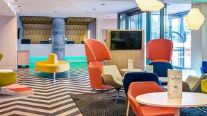 A modern lounge area with colorful seating, a large flat-screen TV, and a patterned floor.