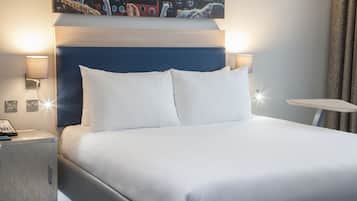 A hotel room with a large bed, two bedside lamps, a small table, and a wall-mounted artwork.