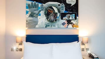 A bedroom with a large bed, two bedside lamps, and a wall-mounted painting of an astronaut taking a selfie in space.