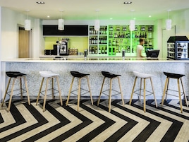 Un área de bar moderna con mostrador, taburetes y una estantería iluminada en verde que exhibe botellas.