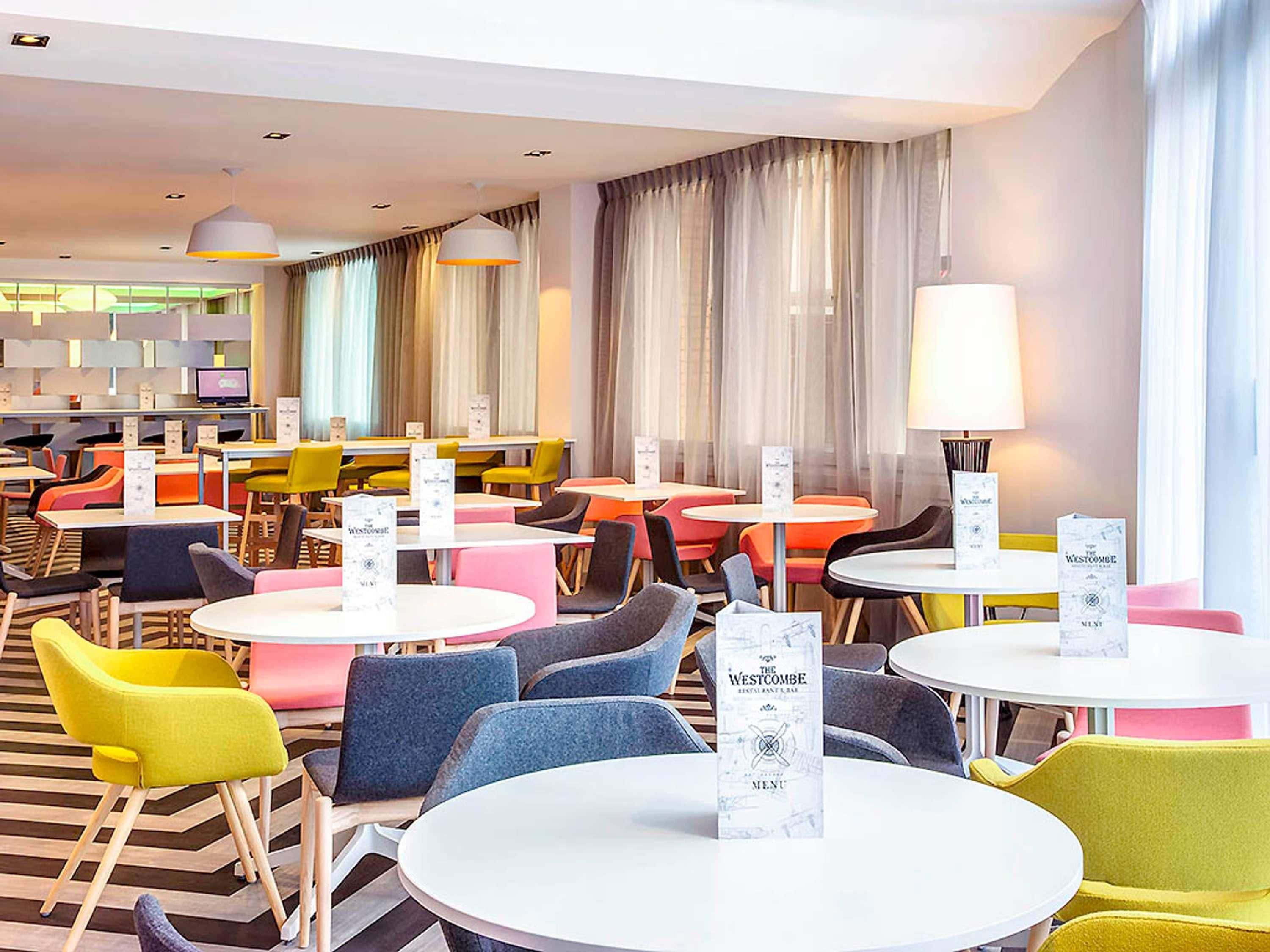 A hotel lobby with round tables, colorful chairs, and a menu stand.
