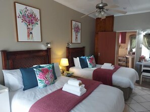 A hotel room with three beds, each with white linens and decorative pillows. There is a ceiling fan, a bedside table with a lamp, and artwork on the walls. - West Street Inn - Ermelo (Ermelo)