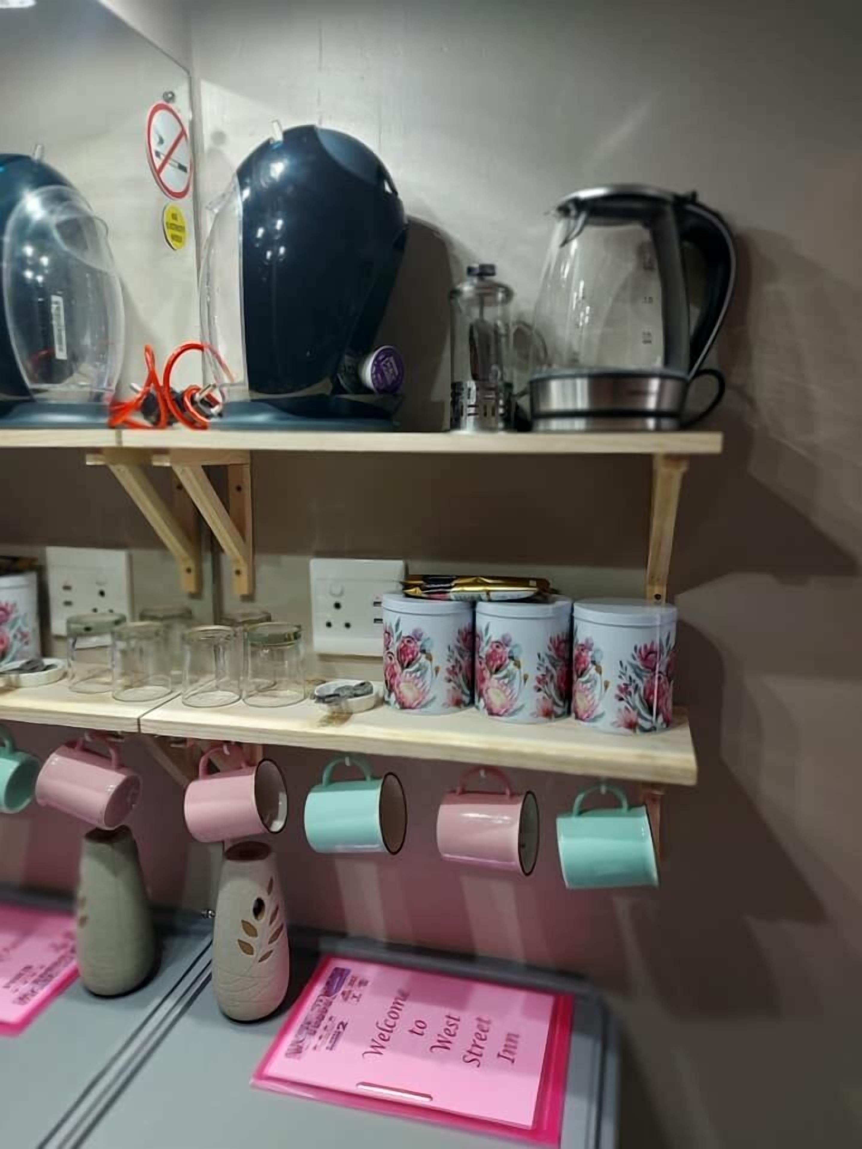 A kitchen with a kettle, a coffee maker, and a set of mugs on a shelf.