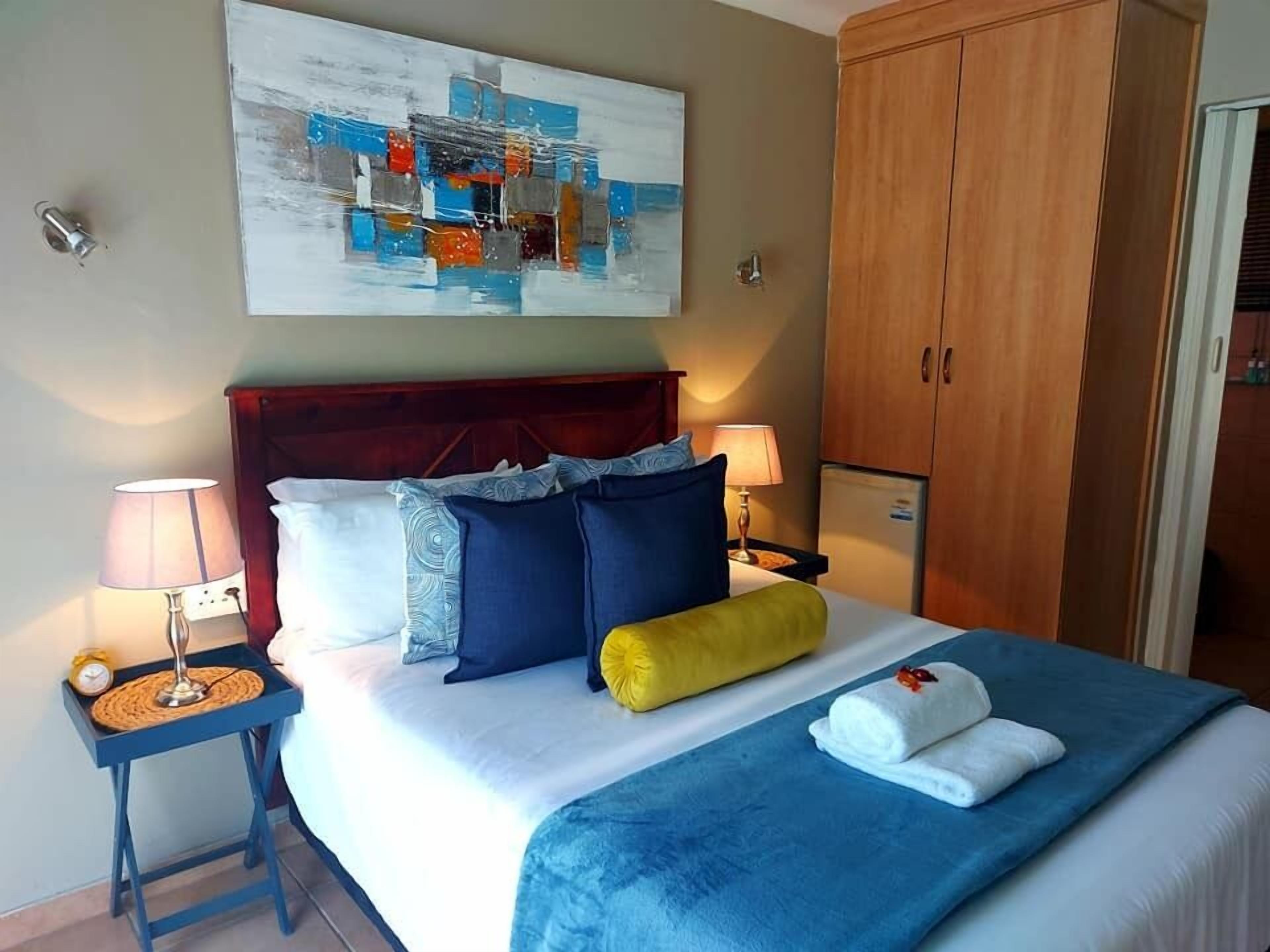 Une chambre d’hôtel avec un grand lit, deux tables de chevet avec des lampes, une armoire en bois et un tableau au mur.