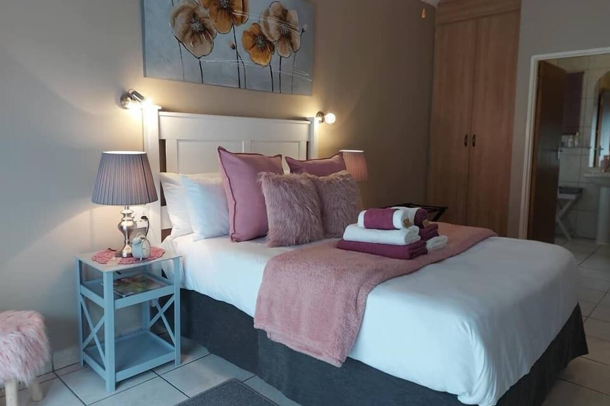 A bedroom with a bed, bedside tables, a nightstand, a fluffy chair, and a painting on the wall.