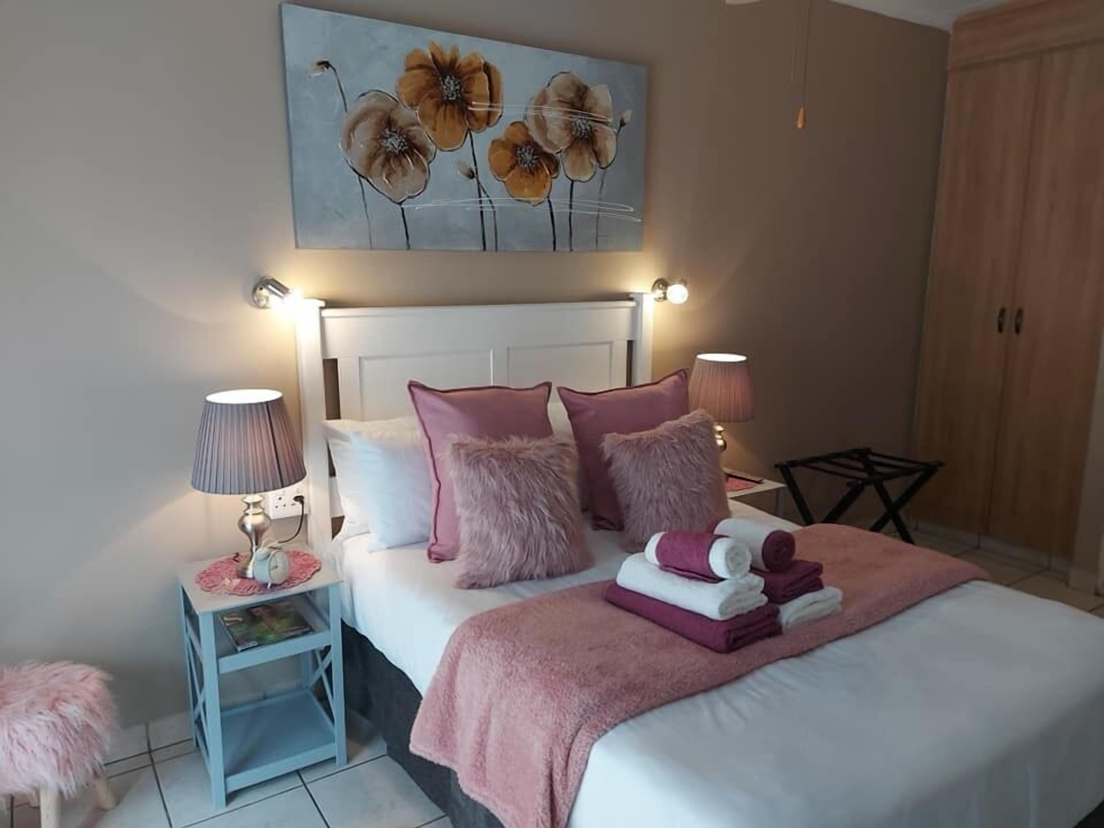 A neatly arranged bedroom with a bed, bedside lamps, a small table, and a fluffy stool.
