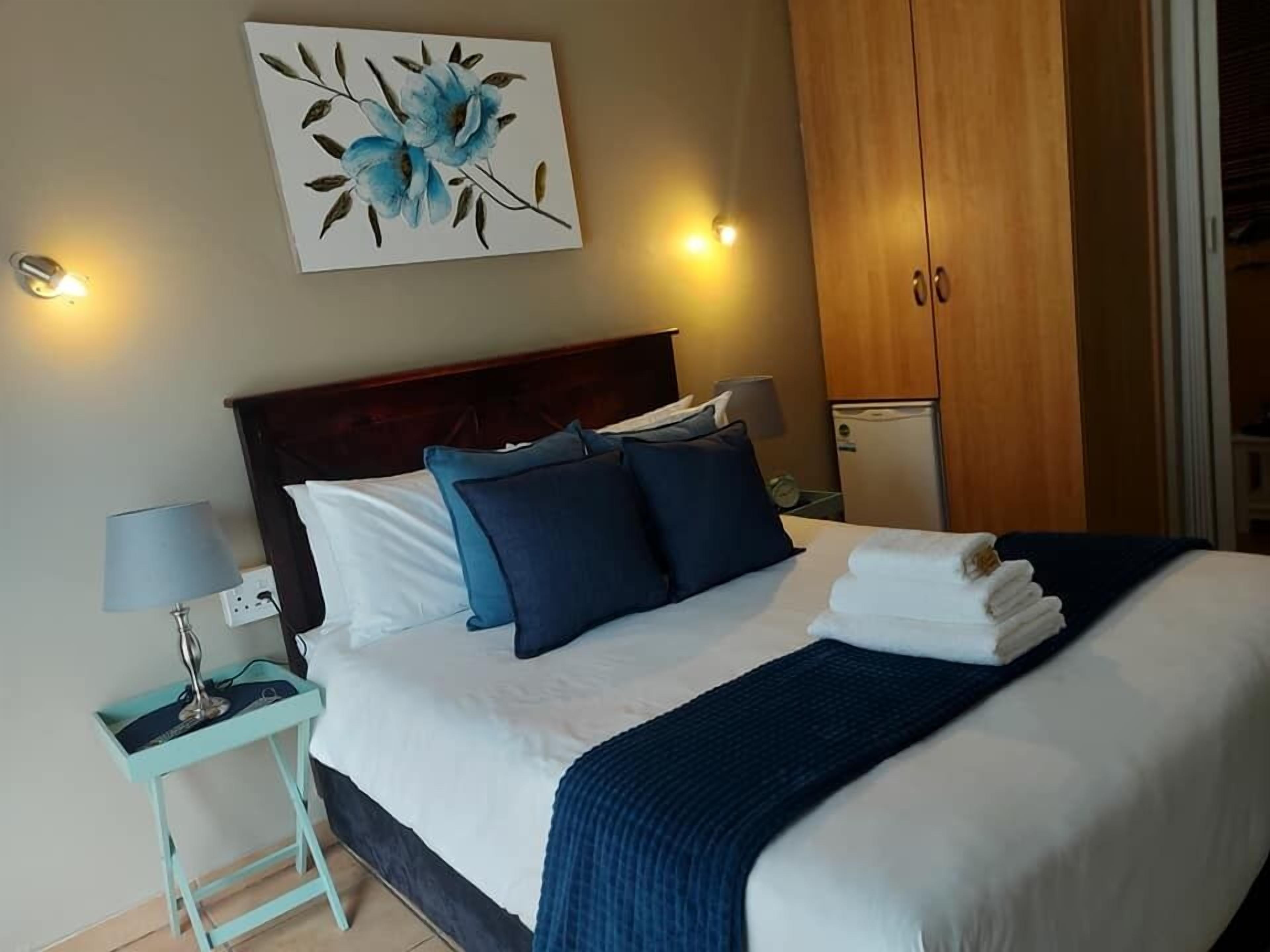 Un lit bien fait, avec une literie bleue, un tableau représentant des fleurs bleues accroché au mur et une armoire en bois.