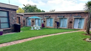 A brick building with numbered rooms, a grassy lawn, and a pathway. - West Street Inn - Ermelo (Ermelo)