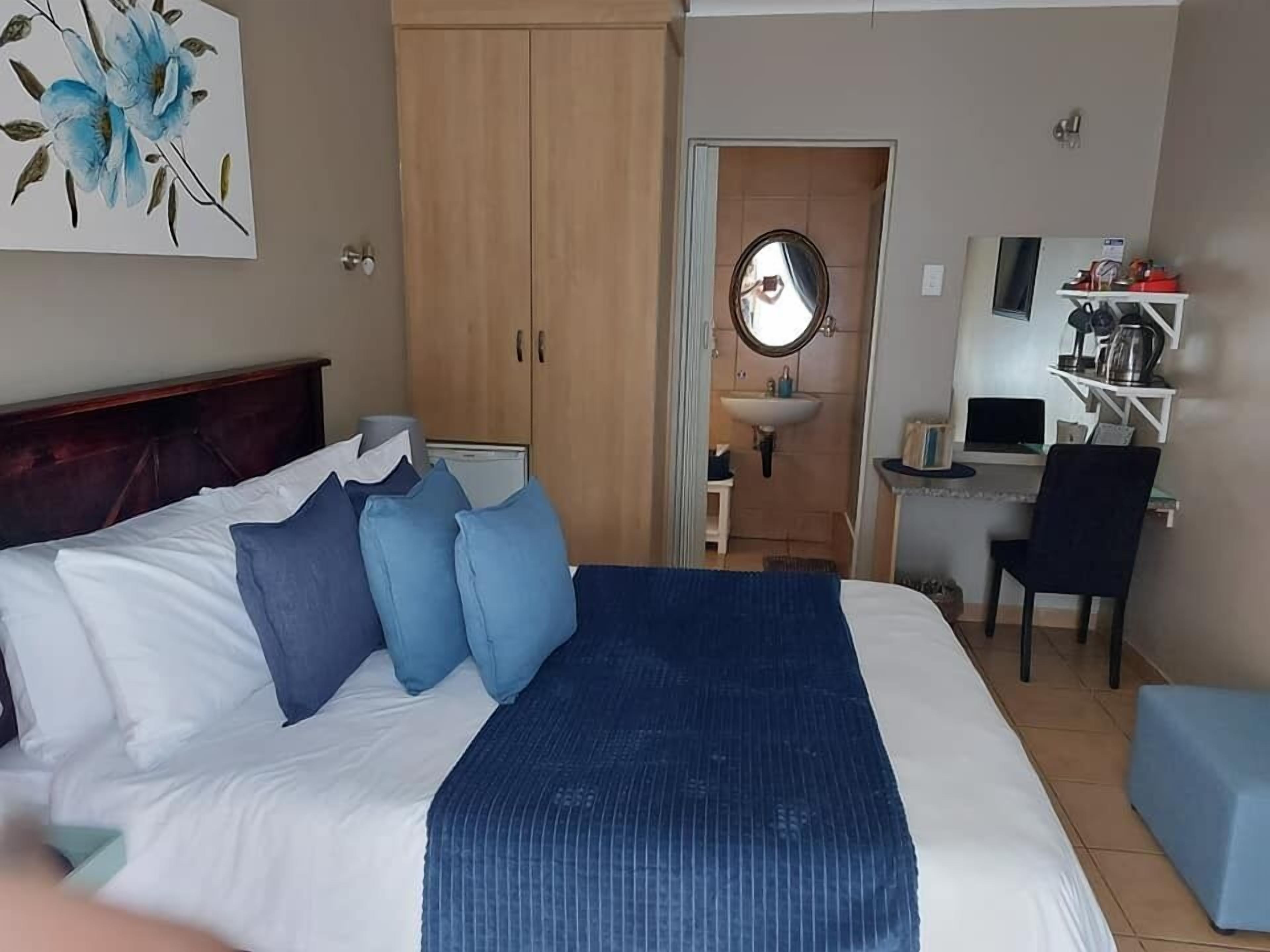 A hotel room with a bed, a desk, a chair, a sink, and a mirror.