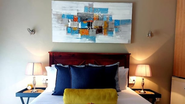 A neatly made bed with blue and white bedding, a wooden headboard, and two bedside lamps. - West Street Inn - Ermelo (Ermelo)