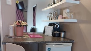 A compact kitchenette with a small refrigerator, a chair, a countertop, and a shelf with kitchen items. - West Street Inn - Ermelo (Ermelo)