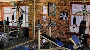 A gym with various exercise equipment, brick walls, and a window with blinds. - West Street Inn - Ermelo (Ermelo)