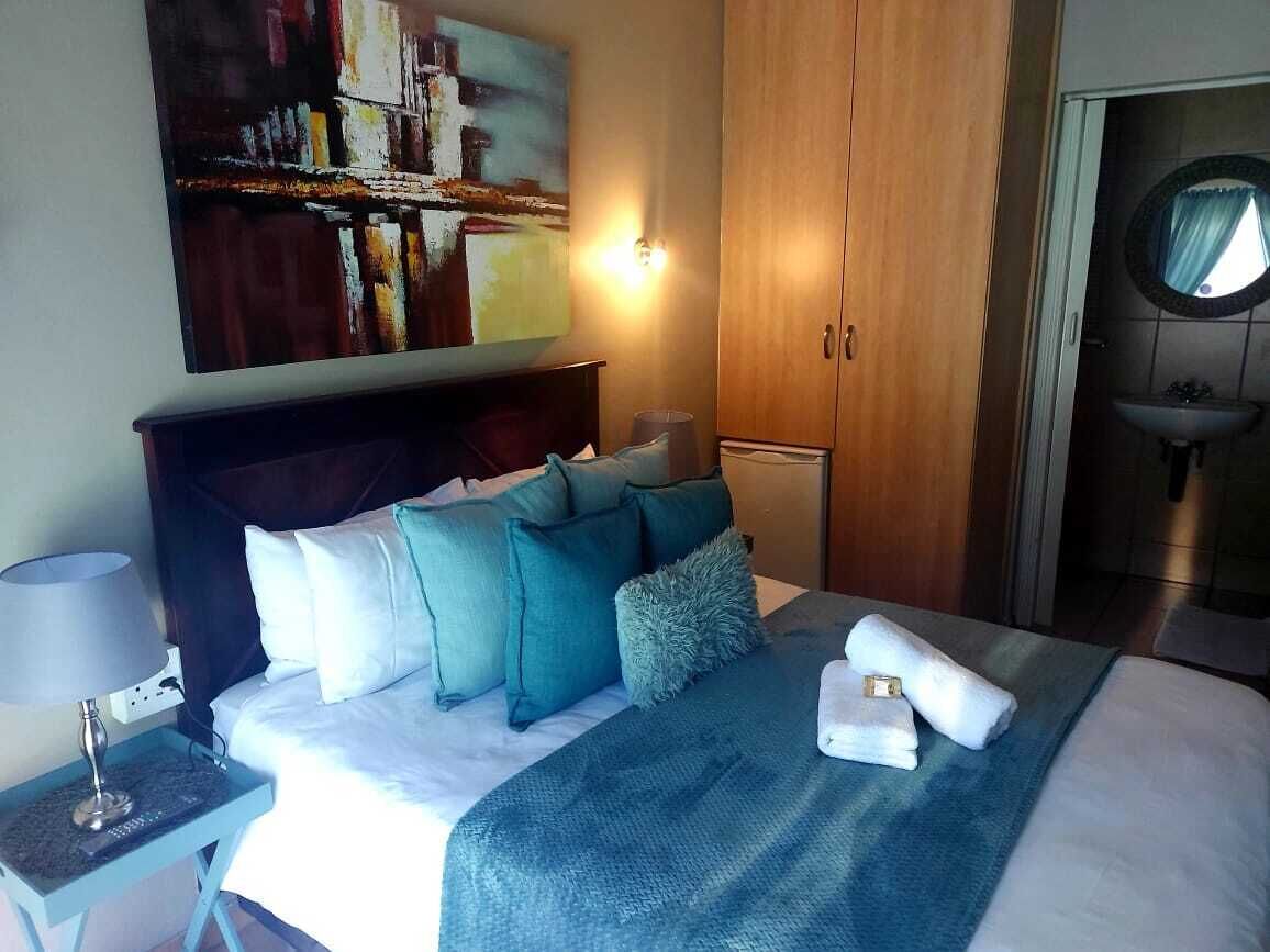 Et hotelværelse med en seng, et natbord med lampe, et billede på væggen, et klædeskab og et badeværelse med vask og spejl.