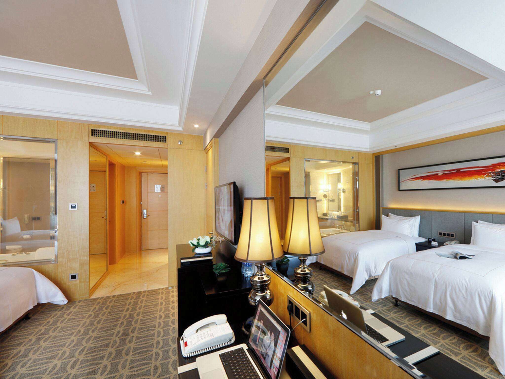 Habitación de hotel con dos camas, un escritorio con teléfono y computadora portátil, un espejo y un cuadro en la pared.