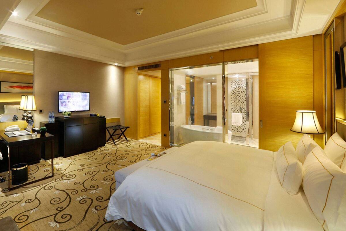 Ein Hotelzimmer mit einem großen Bett, einem Schreibtisch mit Computer, einem Fernseher und einem Badezimmer mit Badewanne und Dusche.