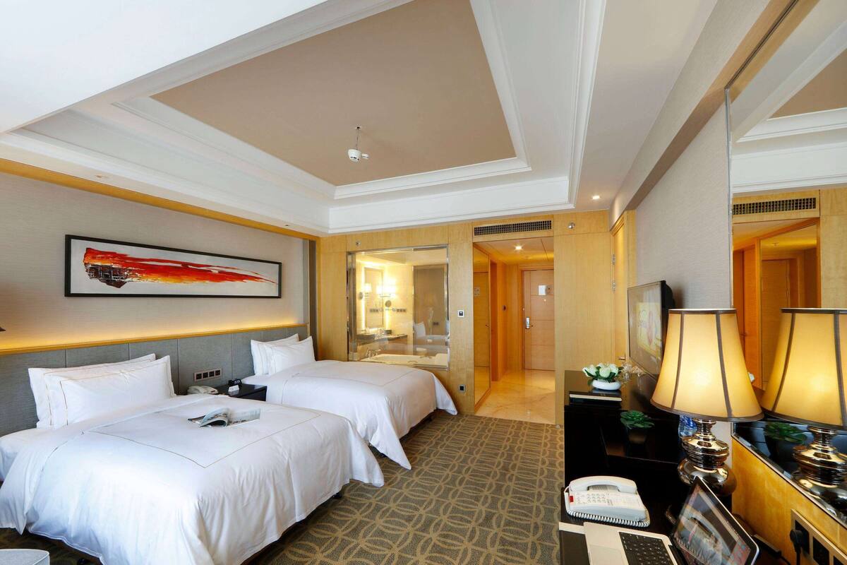 Ein Hotelzimmer mit zwei Betten, einem Schreibtisch mit Lampe, einem Telefon und einem Fernseher.