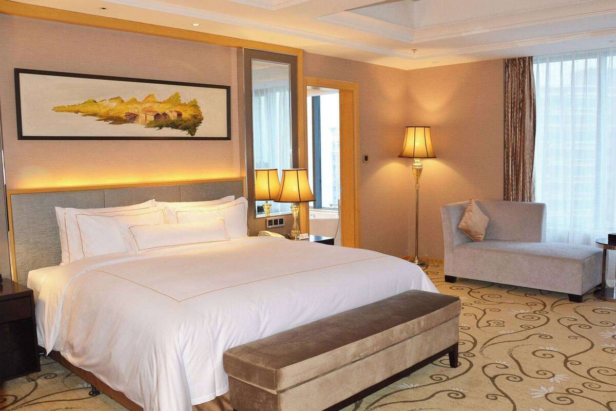 Ein Hotelzimmer mit einem großen Bett, einem Sessel, einer Bank, einem Schreibtisch und einer Lampe.