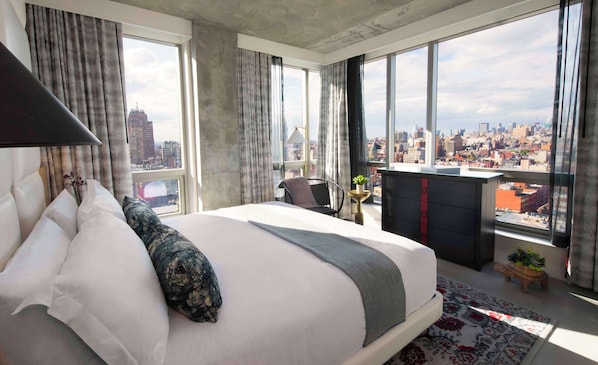 Una habitación de hotel moderna con una cama grande, vistas a la ciudad y un pequeño balcón con plantas.