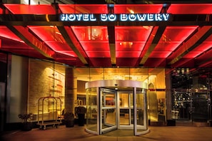 The entrance of Hotel 50 Bowery with a revolving door and a bright red neon sign.