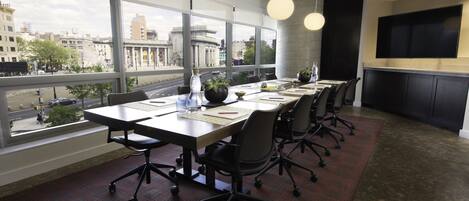 A modern conference room with large windows, a flat-screen TV, and a city view.