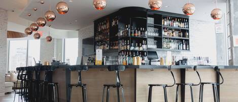 A bar area with a wooden counter, black stools, and a liquor display.
