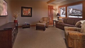 A cozy living room with a fireplace, a comfortable sofa, a chair, and a television. - Storm Peak Chalet At Ski Time (Steamboat Springs)