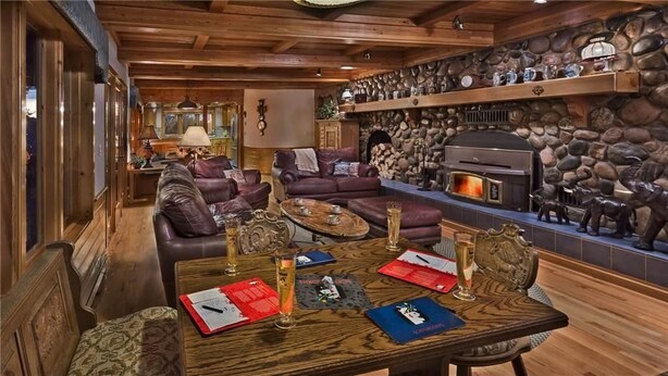 Un salon chaleureux avec une cheminée en pierre, des canapés en cuir et une table basse en bois agrémentée de sets de table rouges et bleus.